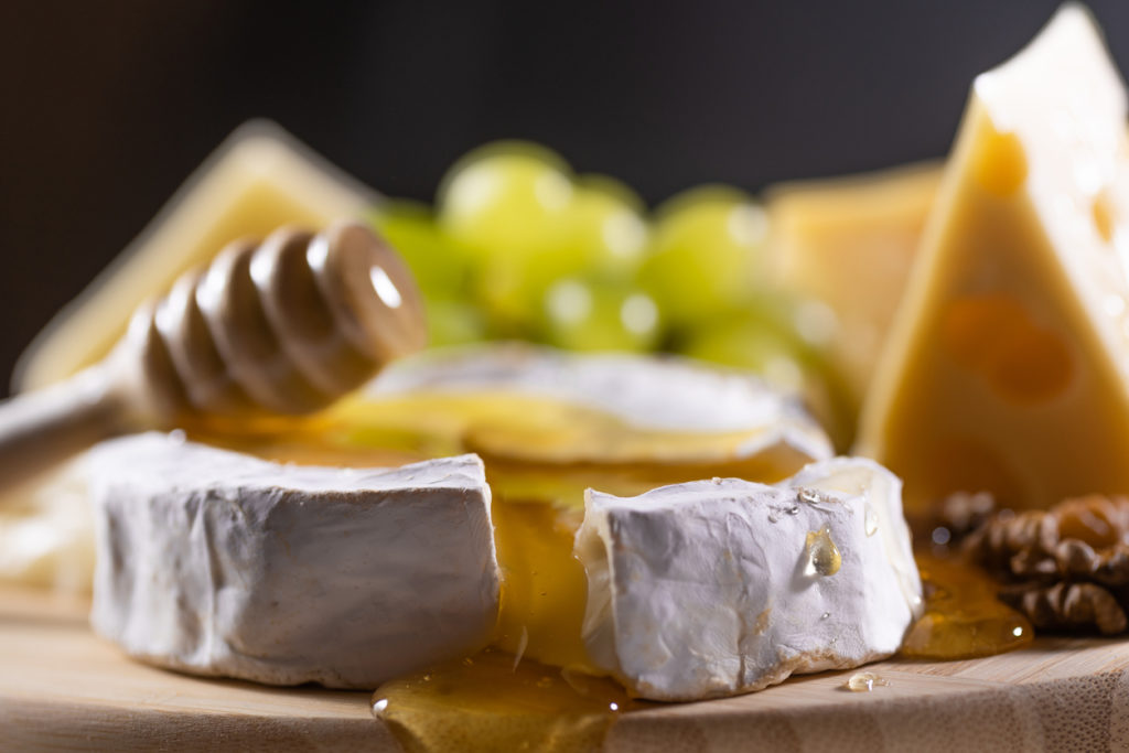 Cheese plate, and honey pouring on camembert cheese.